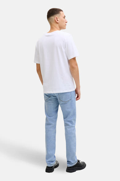 Jean slim bleu clair de JACK & JONES JEANS INTELLIGENCE, porté avec un t-shirt blanc et des chaussures noires, vue de dos.

