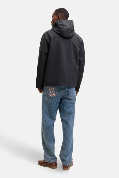 Korte grijze jas van ORIGINALS BY JACK & JONES, met capuchon en patch op de mouw, gedragen met een wijde jeans.