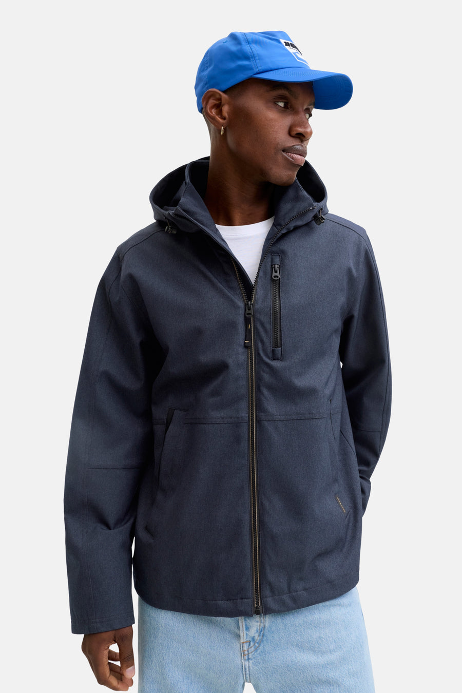 Veste courte bleue par ORIGINALS BY JACK & JONES, avec capuche et fermeture éclair, portée avec un t-shirt blanc et une casquette bleue.