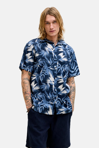 Blauw overhemd met korte mouwen van JACK & JONES, met een tropisch bladerpatroon, gedragen met een korte broek en loafers.