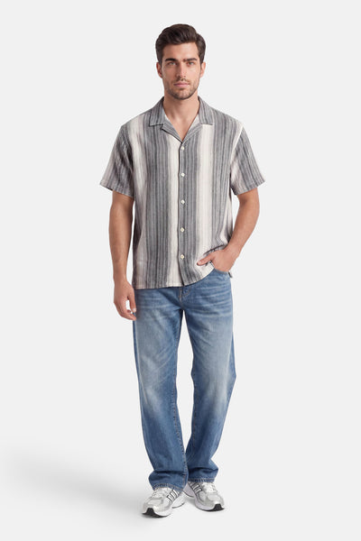 Chemise multicolore à manches courtes de ORIGINALS BY JACK & JONES, à rayures verticales grises et blanches, portée par un homme avec un jean bleu et des baskets argentées.