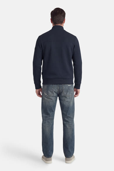 Korte blauwe jas van JACK & JONES, van achteren gezien, gedragen met een lichtgewassen spijkerbroek en grijze sneakers.