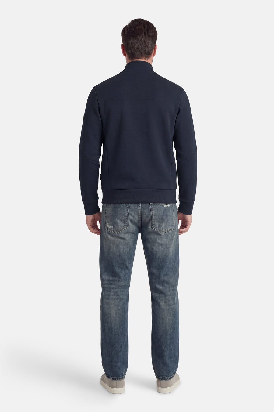 Korte blauwe jas van JACK & JONES, van achteren gezien, gedragen met een lichtgewassen spijkerbroek en grijze sneakers.