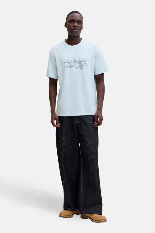 T-shirt bleu à manches courtes par PREMIUM by JACK & JONES, porté avec un pantalon ample et des chaussures marron.
