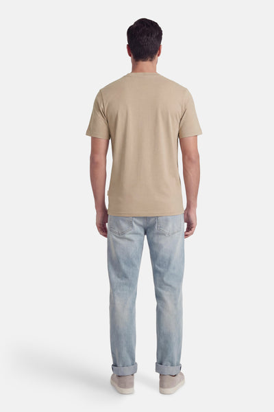 Beige T-shirt met korte mouwen van PREMIUM by JACK & JONES, gedragen met een lichtblauwe jeans en grijze sportschoenen.