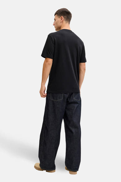 T-shirt noir à manches courtes de JACK & JONES, vu de dos, porté avec un jean ample bleu foncé et des chaussures couleur sable.