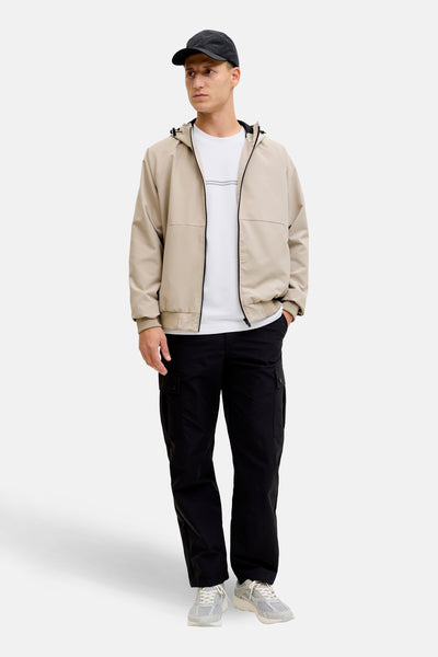 T-shirt à manches courtes blanc de JACK & JONES, porté avec une veste beige à capuche et un pantalon cargo noir.