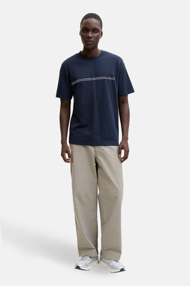 T-shirt à manches courtes bleu marine de JACK & JONES, avec deux rayures horizontales sur le devant et un pantalon beige.