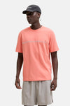 T-shirt orange à manches courtes de JACK & JONES avec deux lignes horizontales sur la poitrine, porté avec un short gris et une casquette noire.