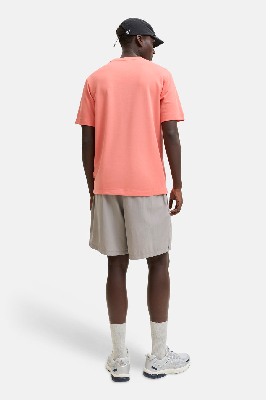 T-shirt à manches courtes orange de JACK & JONES porté de dos avec un short gris et une casquette noire.