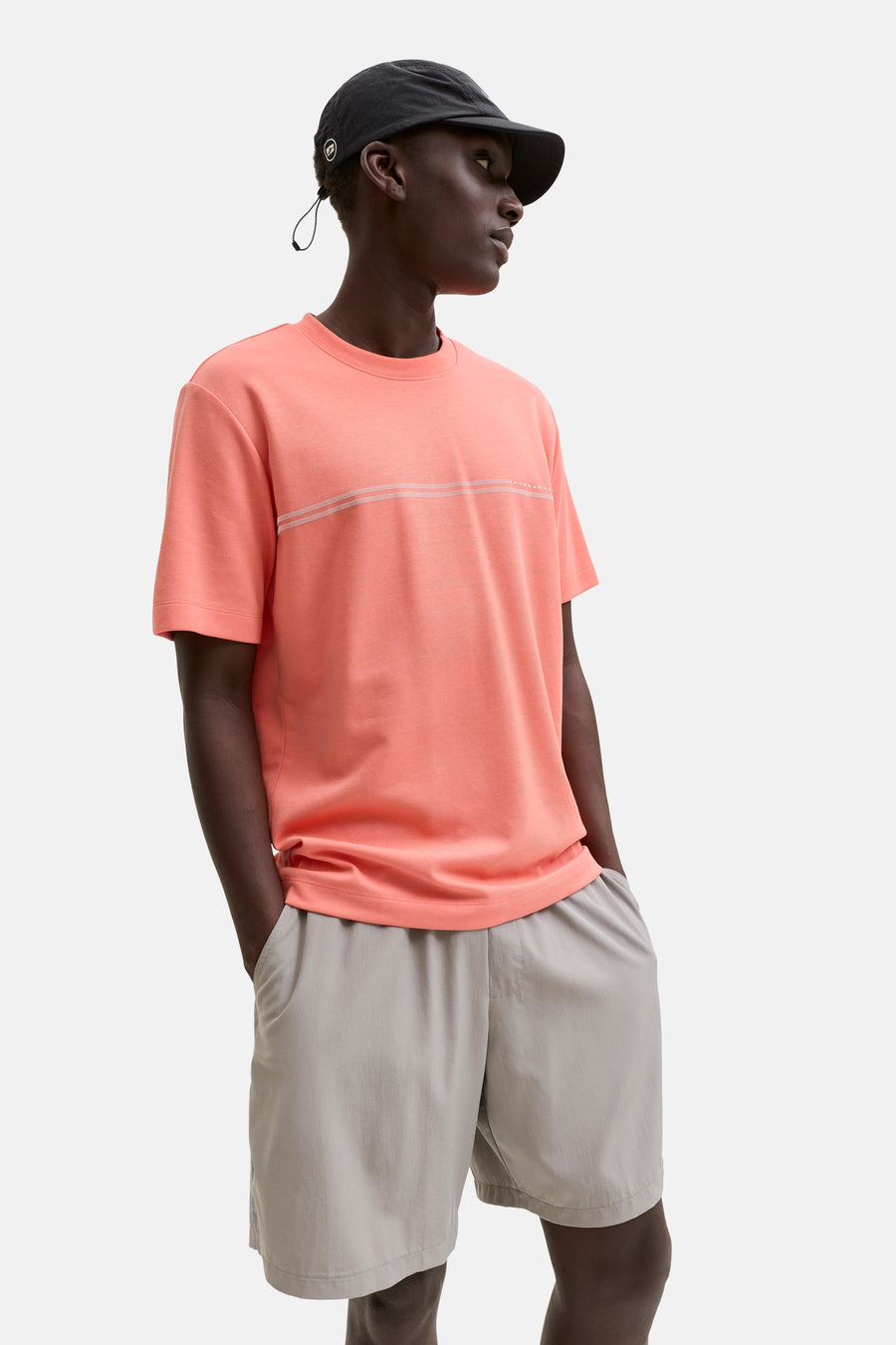 T-shirt orange de JACK & JONES avec deux fines lignes blanches et le logo discret sur la poitrine, porté avec un short gris clair et une casquette noire.