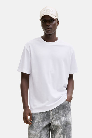 Wit T-shirt van JACK & JONES, gedragen met een beige hoed en een grijs-witte verweerde broek.