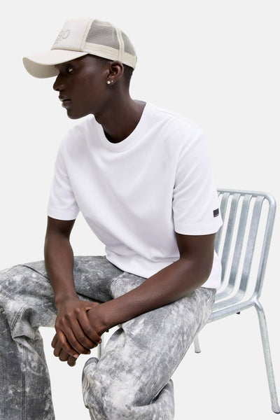 Wit T-shirt met korte mouwen van JACK & JONES, gedragen met een verweerde broek met patroon en een beige pet.