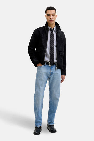Jean tapered en denim bleu clair de Jack & Jones Jeans Intelligence, porté avec une veste noire et une cravate rayée.
