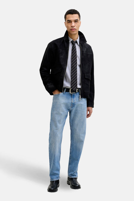 Jean tapered en denim bleu clair de Jack & Jones Jeans Intelligence, porté avec une veste noire et une cravate rayée.
