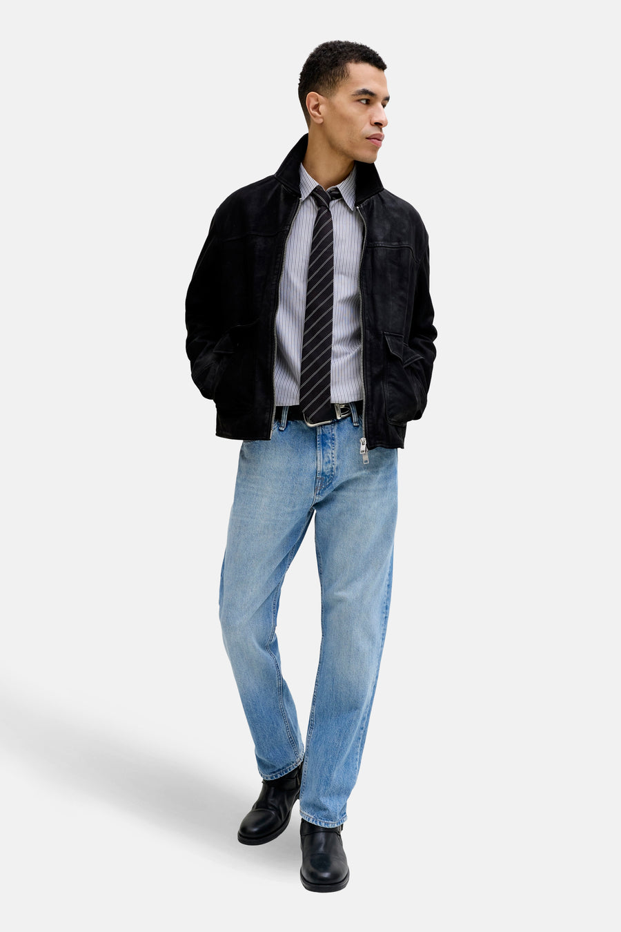 Jean fuselé en denim bleu clair de JACK & JONES JEANS INTELLIGENCE, porté avec une chemise rayée, une cravate et une veste zippée.