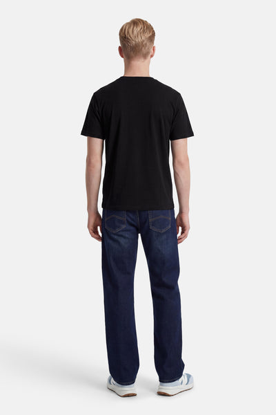 T-shirt noir à manches courtes d'ORIGINALS BY JACK & JONES porté de dos avec un jean bleu foncé et des baskets.