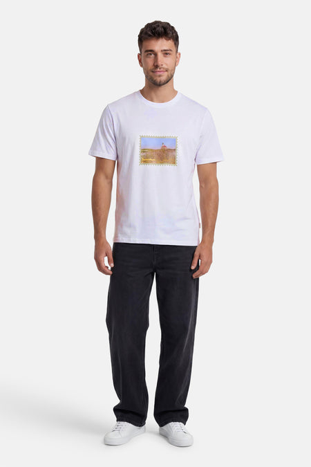 Wit T-shirt van het merk ORIGINALS BY JACK & JONES met landschapstempel en tekstmotief, gedragen met een donkere spijkerbroek en witte sneakers.