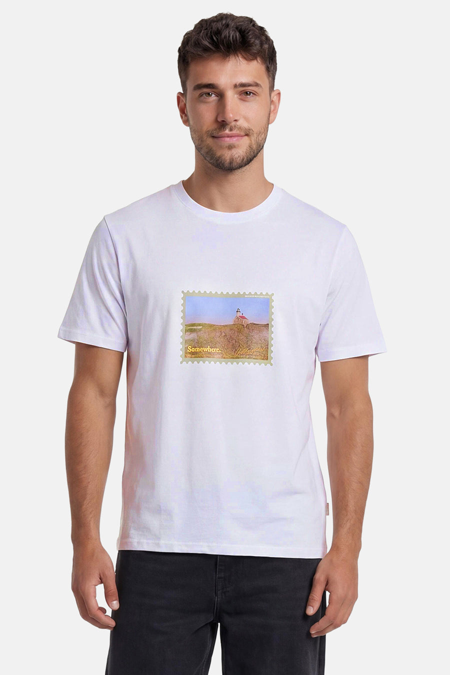 T-shirt blanc d'ORIGINALS BY JACK & JONES avec un motif de timbre-poste représentant un phare et l'inscription "Somewhere.", porté par un homme en jean noir.