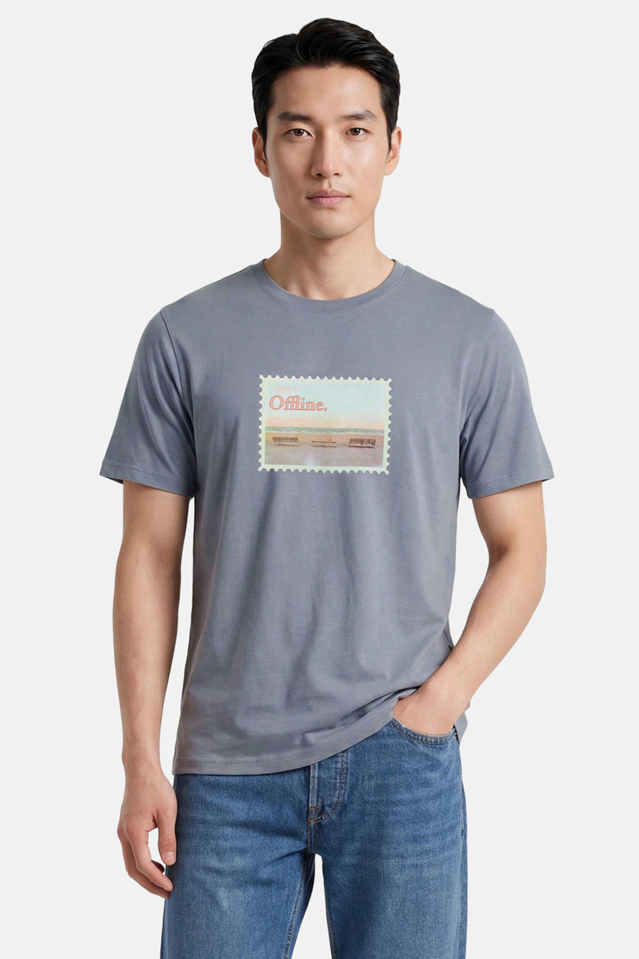 T-shirt gris-bleu à manches courtes de ORIGINALS BY JACK & JONES avec imprimé timbre "Offline." et scène de plage, porté par un homme en jeans.