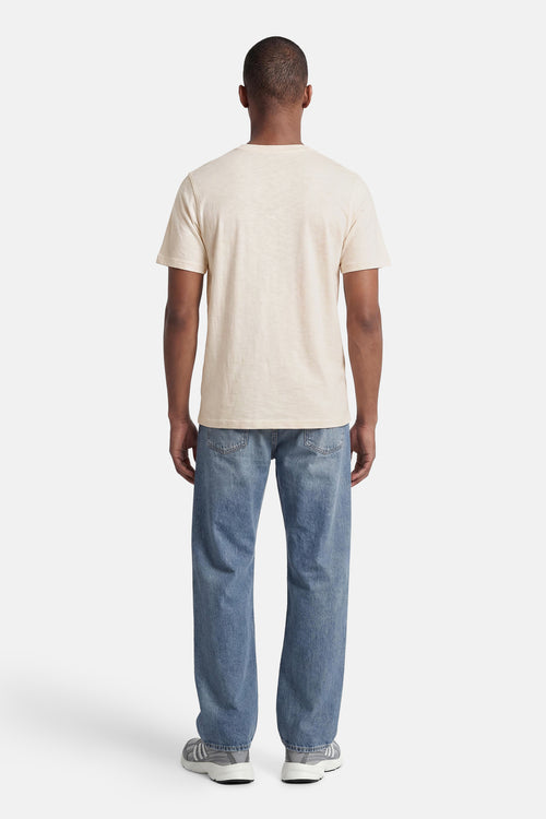 T-shirt beige clair de PREMIUM by JACK & JONES, vu de dos avec manches courtes, porté avec un jean bleu et des baskets grises.