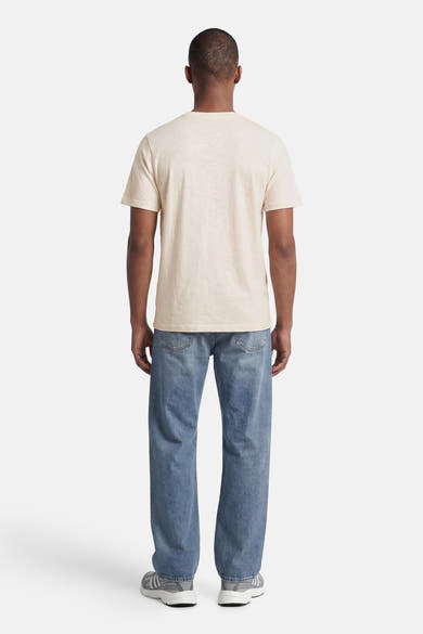 Lichtbeige T-shirt van PREMIUM by JACK & JONES, van achteren gezien met korte mouwen, gedragen met een blauwe jeans en grijze sneakers.