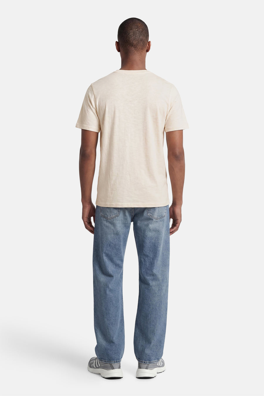 Lichtbeige T-shirt van PREMIUM by JACK & JONES, van achteren gezien met korte mouwen, gedragen met een blauwe jeans en grijze sneakers.