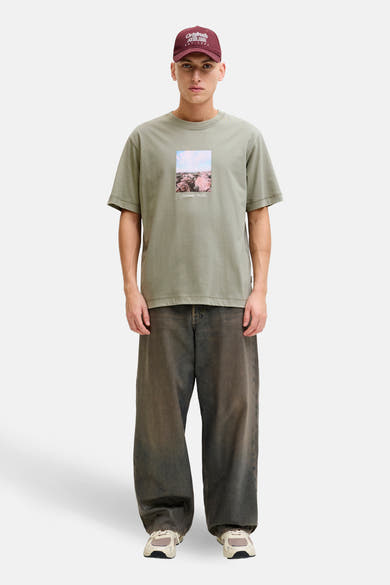 Groen T-shirt met korte mouwen van ORIGINALS BY JACK & JONES, met een landschapsprint, gedragen met een wijde broek en een bordeauxrode pet.