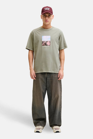 Groen T-shirt met korte mouwen van ORIGINALS BY JACK & JONES, met een landschapsprint, gedragen met een wijde broek en een bordeauxrode pet.