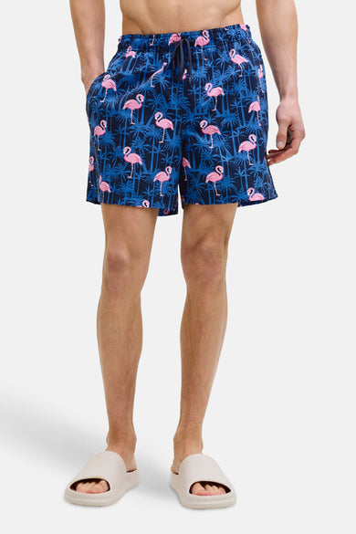 Blauwe zwembroek met roze flamingo-print van JACK & JONES JEANS INTELLIGENCE, gedragen met beige sandalen.