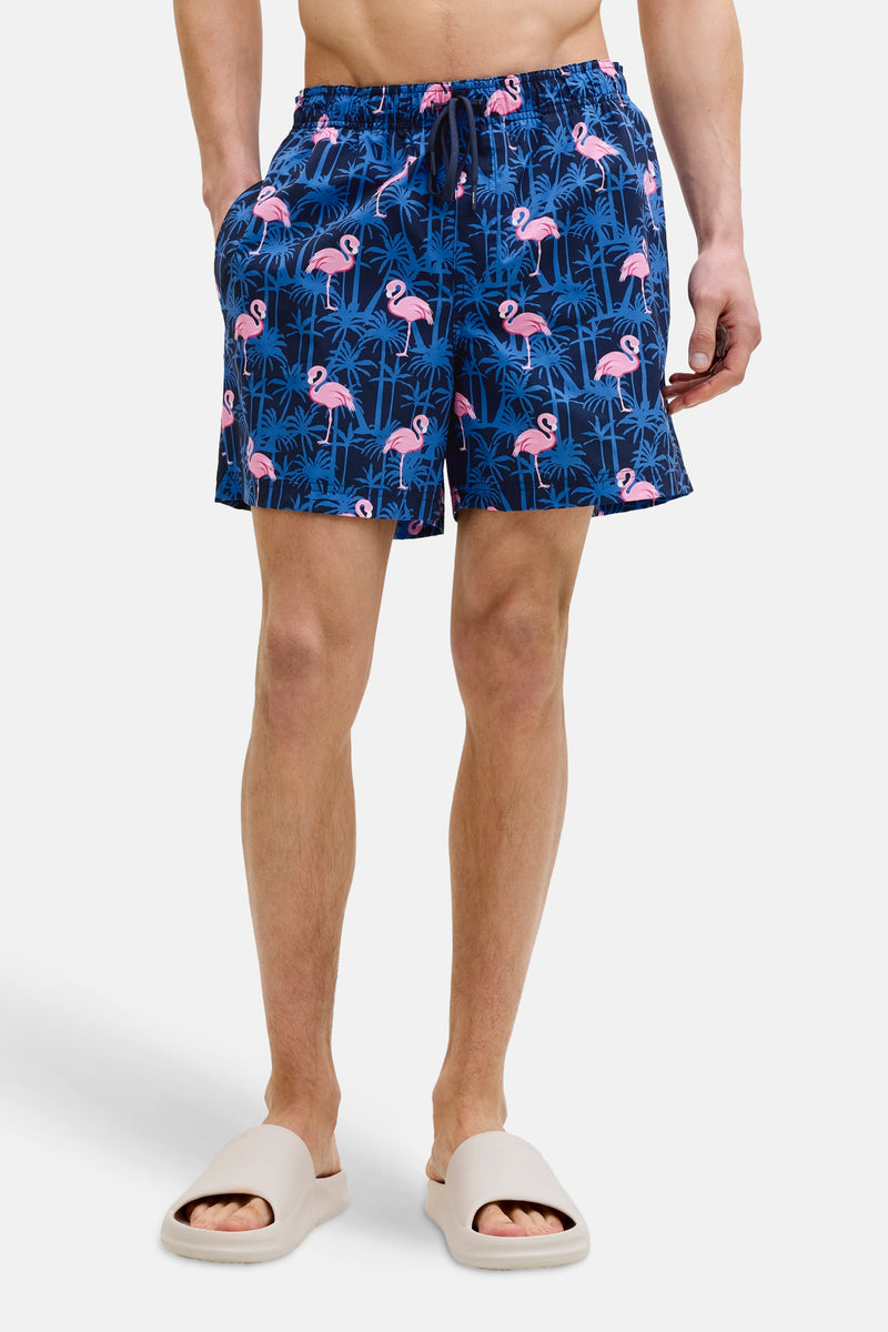 Blauwe zwembroek met roze flamingo-print van JACK & JONES JEANS INTELLIGENCE, gedragen met beige sandalen.