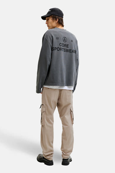 Beige cargobroek van JACK & JONES, gedragen met een grijs bedrukt sweatshirt en dikke zwarte schoenen.