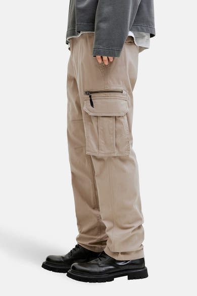 Beige cargobroek van JACK & JONES, met zijzakken met rits, gedragen met zwarte schoenen.