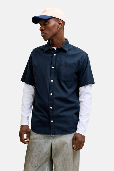 Chemise bleue à manches courtes de JACK & JONES, portée sur un t-shirt blanc à manches longues et un jean délavé.