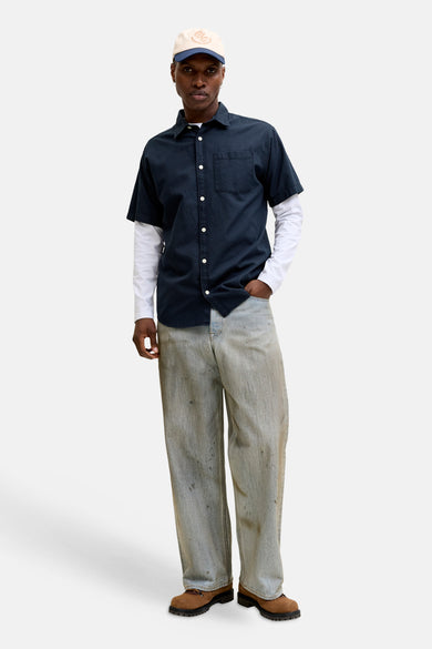 Chemise bleue à manches courtes de JACK & JONES, avec texture subtile, portée sur un t-shirt blanc à manches longues et un pantalon décontracté.