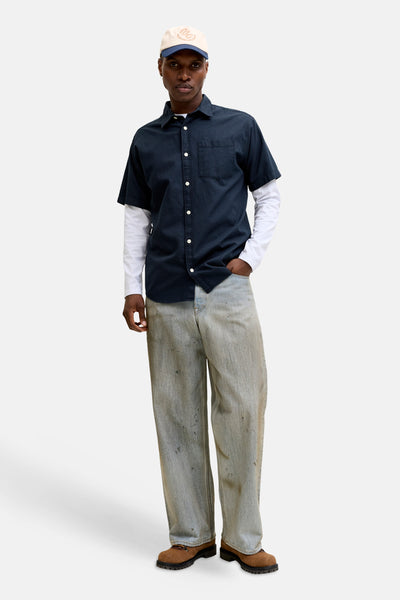 Chemise bleue à manches courtes de JACK & JONES, avec texture subtile, portée sur un t-shirt blanc à manches longues et un pantalon décontracté.