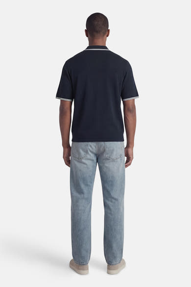 Polo bleu à manches courtes de JACK & JONES, avec finitions à rayures blanches au col et aux manches, porté avec un jean décontracté.