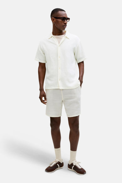 Chemise blanche à manches courtes par ORIGINALS BY JACK & JONES, texturée, portée avec un t-shirt et un short assortis.