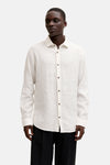 Chemise en lin blanc de PREMIUM by JACK & JONES avec boutons marron, portée avec un pantalon rayé.