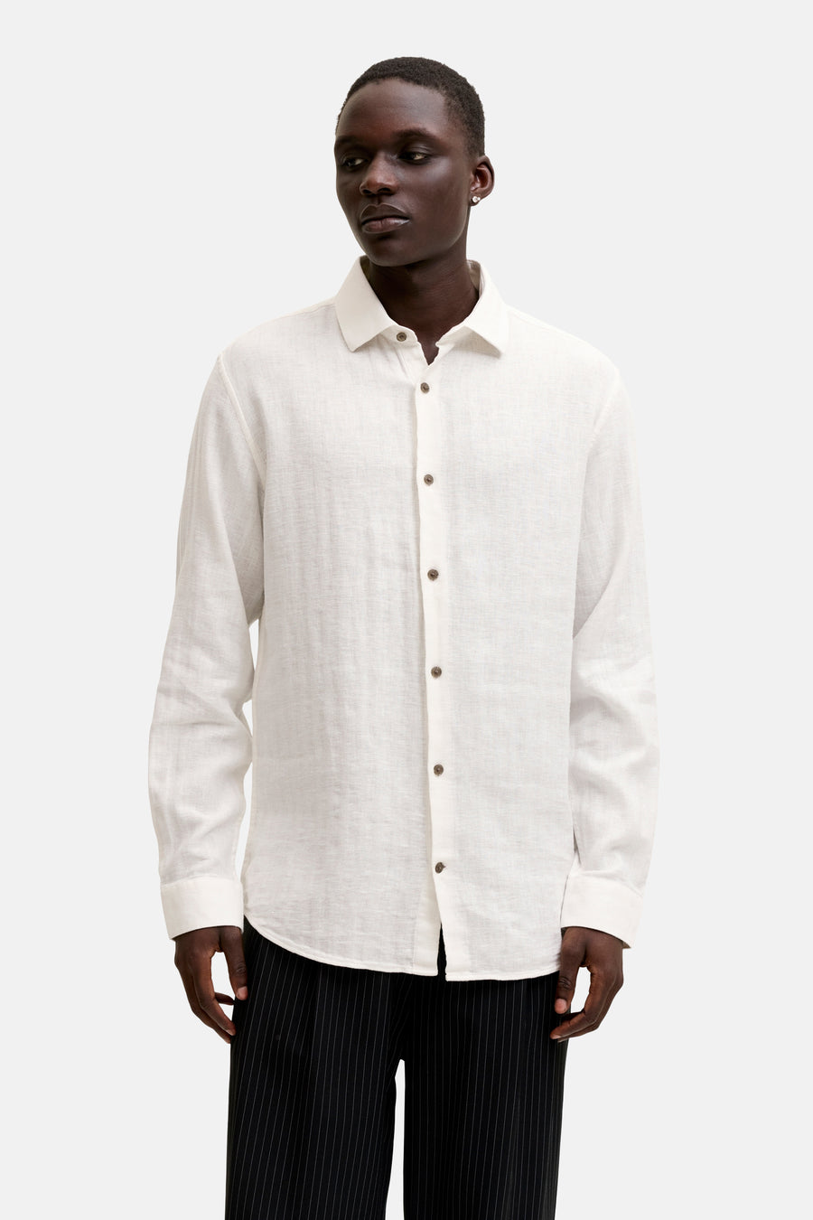 Chemise en lin blanc de PREMIUM by JACK & JONES avec boutons marron, portée avec un pantalon rayé.