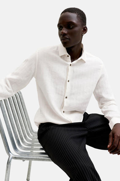 Chemise blanche à manches longues de PREMIUM by JACK & JONES, texturée avec boutons marron, portée par un homme assis.