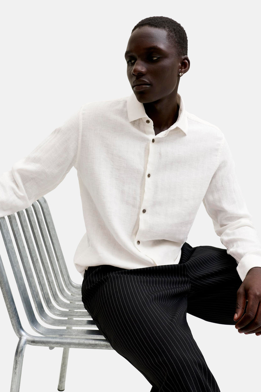 Chemise blanche à manches longues de PREMIUM by JACK & JONES, texturée avec boutons marron, portée par un homme assis.