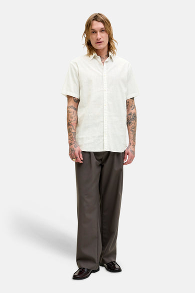 Chemise à manches courtes blanche à motifs, par PREMIUM by JACK & JONES, portée avec un pantalon marron ample et des mocassins.