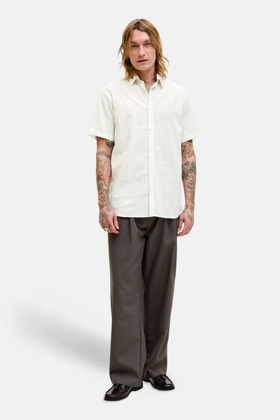 Chemise à manches courtes blanche à motifs, par PREMIUM by JACK & JONES, portée avec un pantalon marron ample et des mocassins.