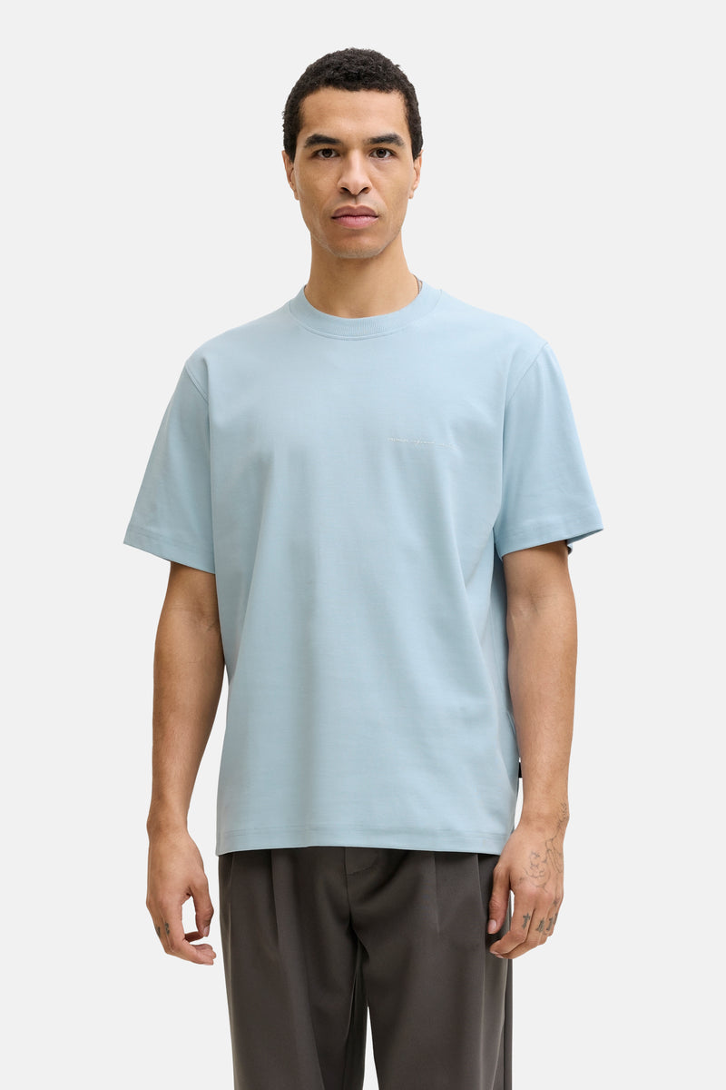 Blauw T-shirt met korte mouwen van PREMIUM by JACK & JONES, gedragen met een grijze broek en bruine loafers.