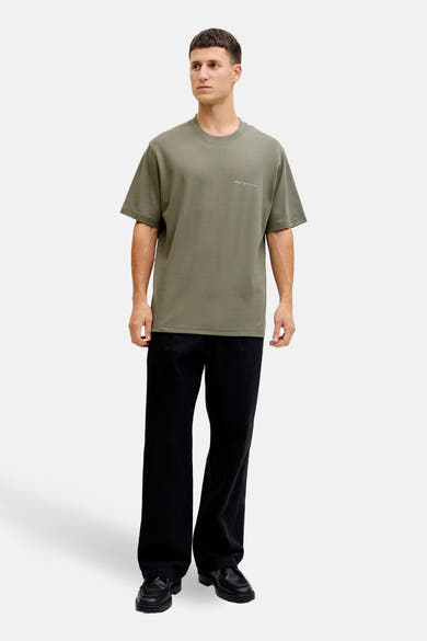 T-shirt kaki à manches courtes de PREMIUM by JACK & JONES, porté avec un pantalon noir ample et des mocassins.
