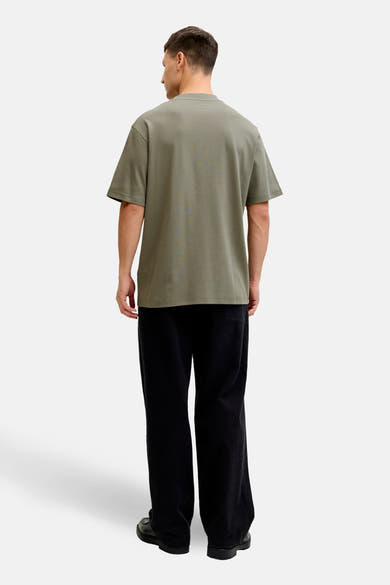Kaki T-shirt met korte mouwen van PREMIUM by JACK & JONES, gedragen met een wijde zwarte broek en zwarte schoenen.