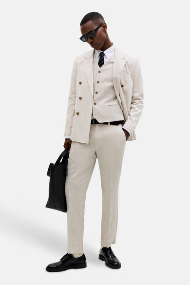Gilet écru en lin de PREMIUM by JACK & JONES, boutonné, porté avec une veste et un pantalon assortis.