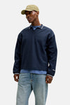 Blauwe trui met ronde hals van ORIGINALS BY JACK & JONES, gedragen met een bruin leren jack, een wijde blauwe jeans en een hoed.