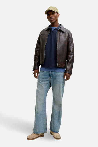 Sweat bleu à col rond par ORIGINALS BY JACK & JONES, porté avec une veste en cuir marron, un jean bleu ample et un chapeau.
